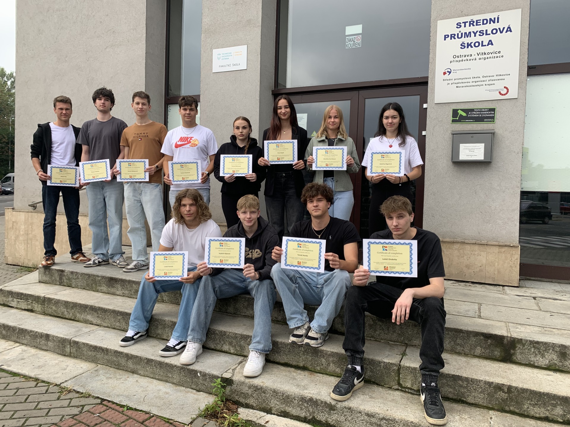 Skupina studentů SPŠ Ostrava pracuje na školním projektu v týmu před vchodem do školy s certifikáty v rukou