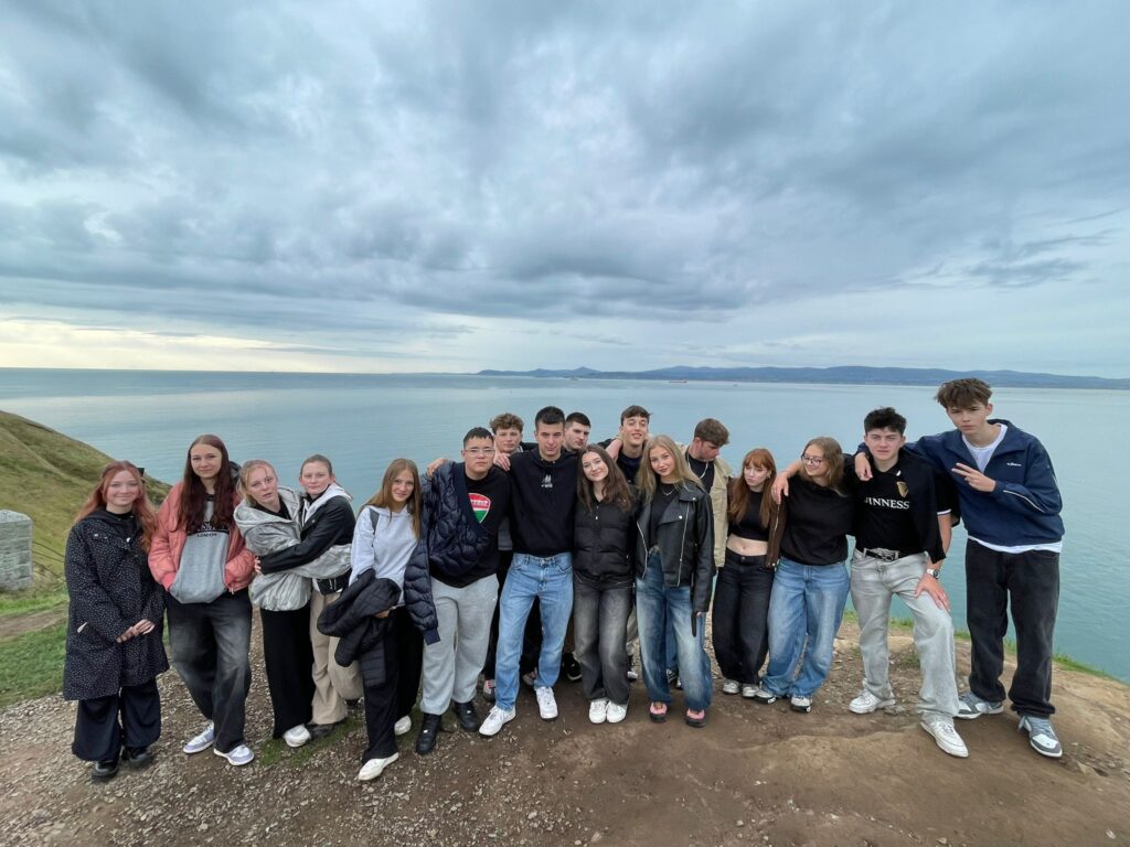 Skupina studentů pózuje na útesu s výhledem na oceán během školního zájezdu do Irska.