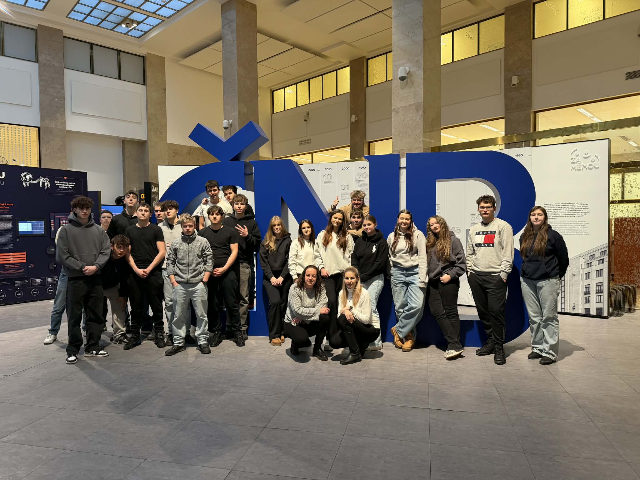 Skupina studentů stojící před velkou modrou instalací s písmeny ČNB uvnitř budovy banky.