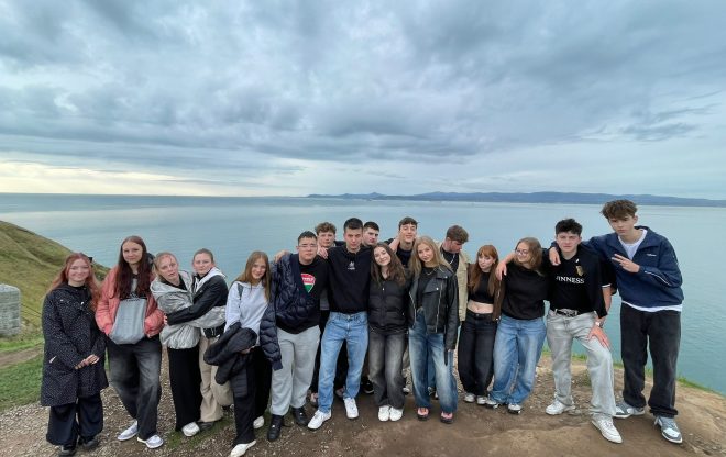 Skupina studentů pózuje na útesu s výhledem na oceán během školního zájezdu do Irska.